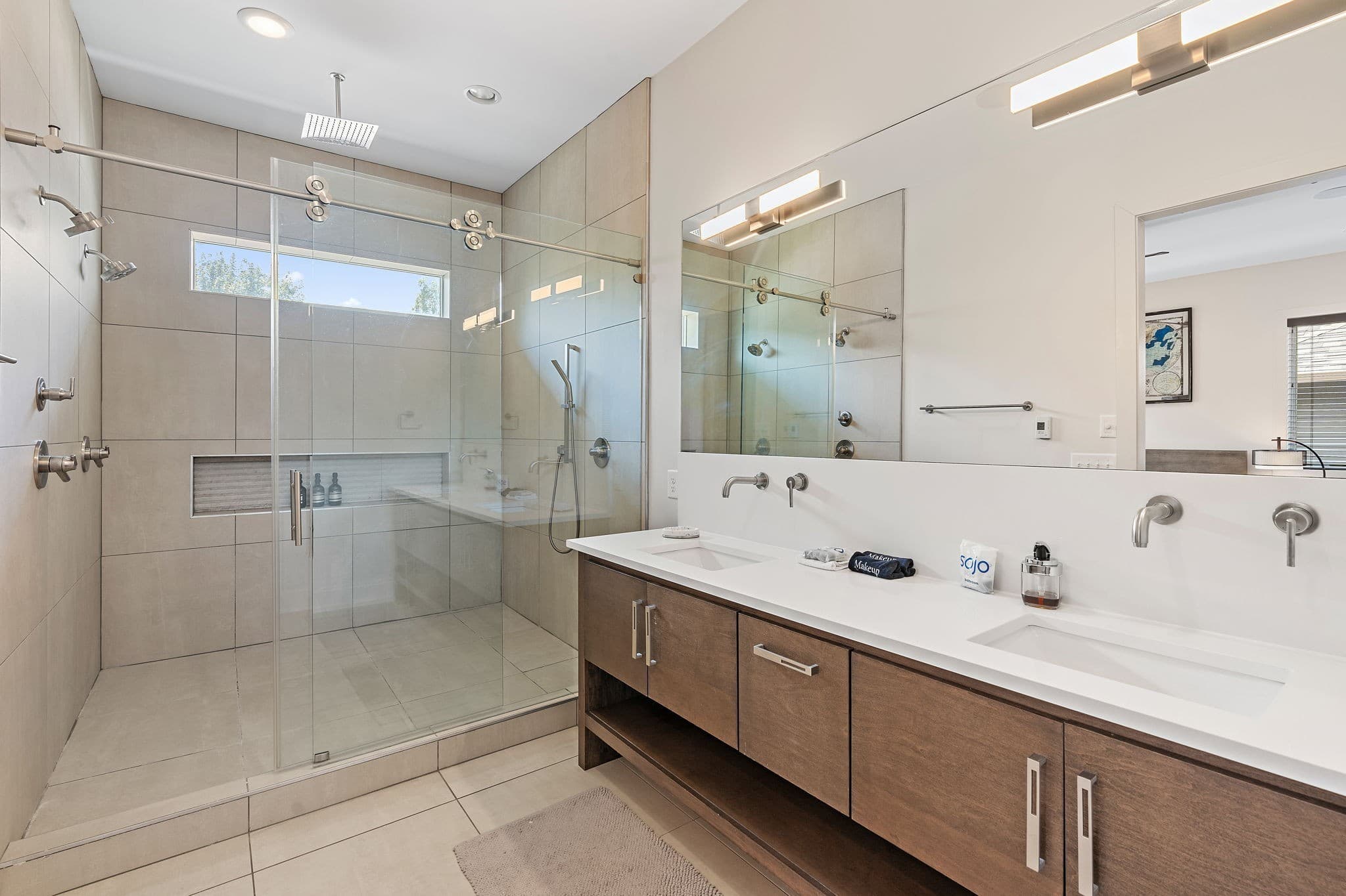 Primary bath with a double vanity on wood cabinets, wall mounted faucets, a wide mirror and a large glass shower with a rain showerhead at 1002 W Grove Avenue in 12 South Nashville