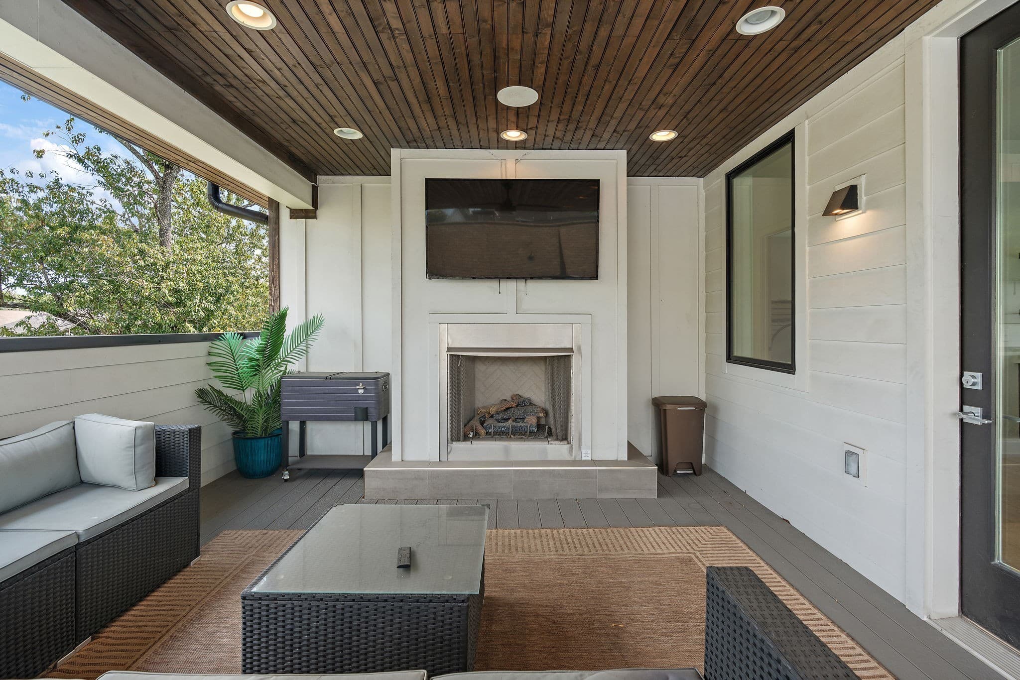 Covered upper terrace with a stained wood ceiling, a fireplace with a TV above it, an outdoor sofa and a coffee table, and treetop views at 1002 W Grove Avenue in 12 South Nashville