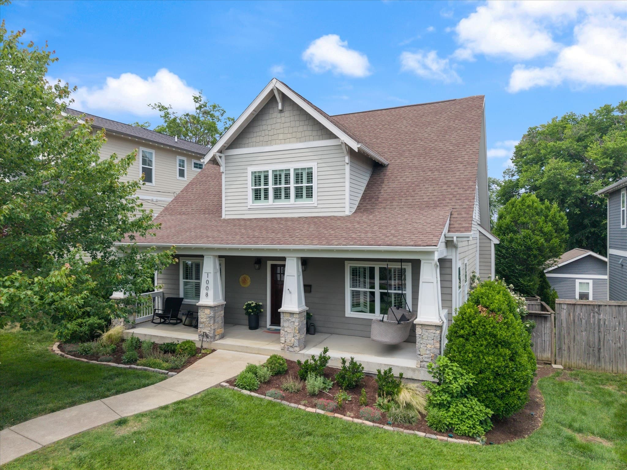 Street view of the front exterior of 1008 Caldwell Avenue, a gray two story home with a covered front porch, stone column bases, the house number 1008 on a porch column, a porch swing, and a walkway across the front lawn, one of the 12 South homes for sale in Nashville