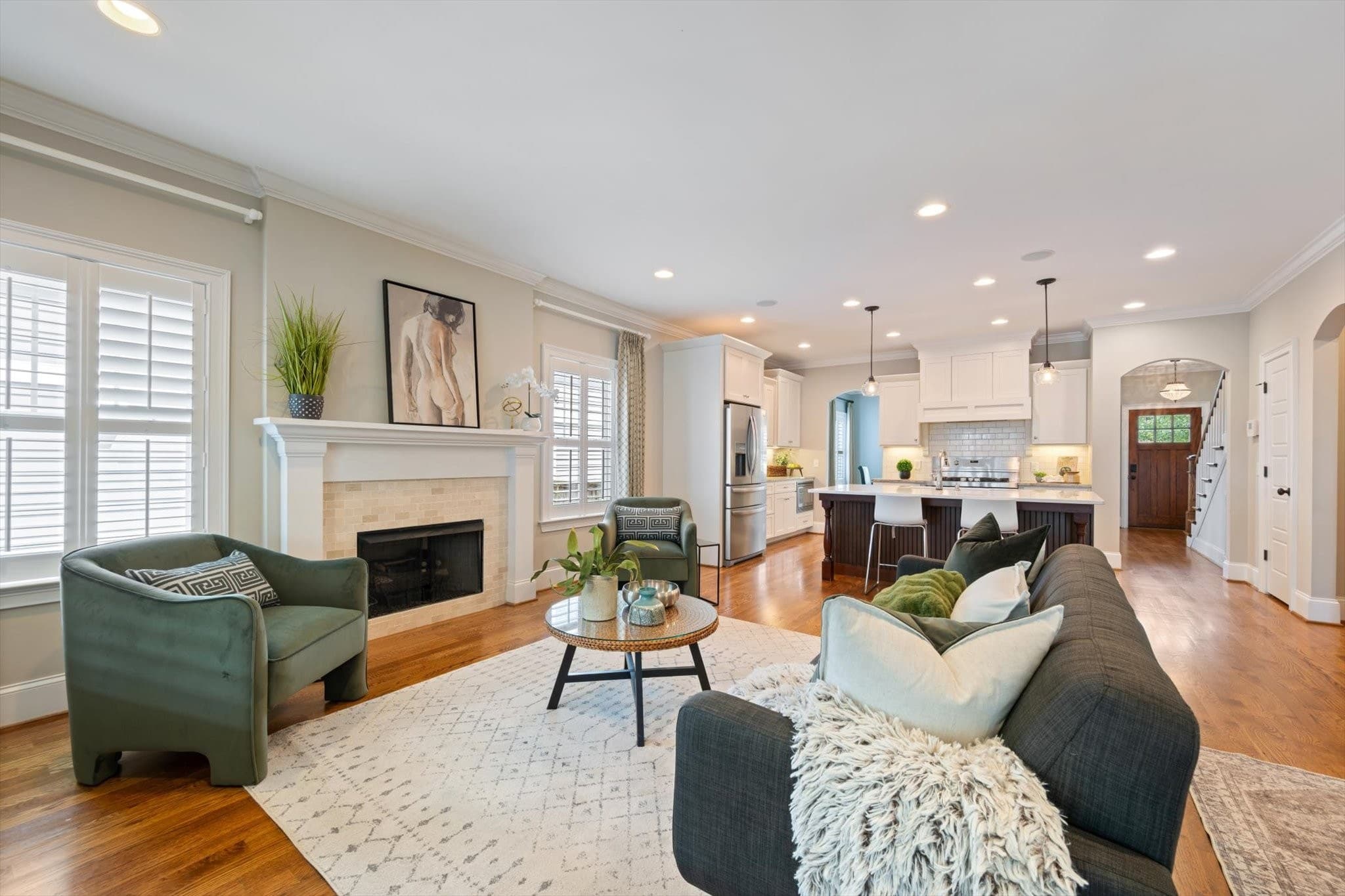 Living room with a tile surround fireplace and white mantel, plantation shutters, and an open view back to the kitchen island and white cabinets at 1008 Caldwell Avenue in 12 South Nashville
