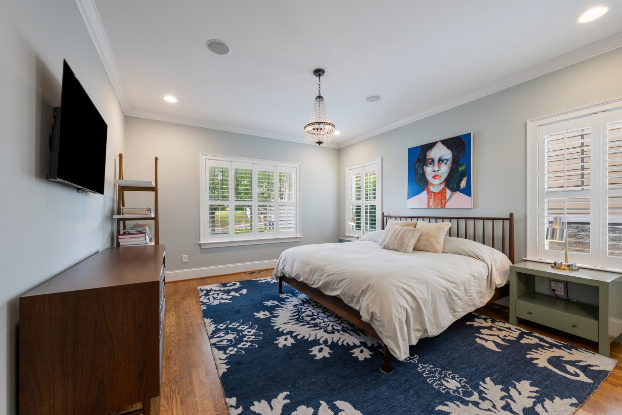 Main level primary bedroom with plantation shutters, a crystal chandelier, hardwood floors, and a navy patterned rug at 1008 Caldwell Avenue in 12 South Nashville