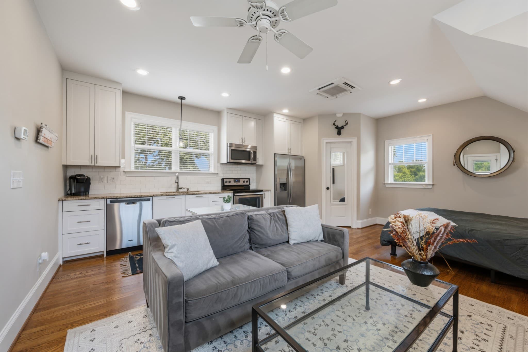 Detached DADU living area with a kitchen of white cabinets and stainless appliances, a gray sofa, and a sleeping area at 1008 Caldwell Avenue in 12 South Nashville