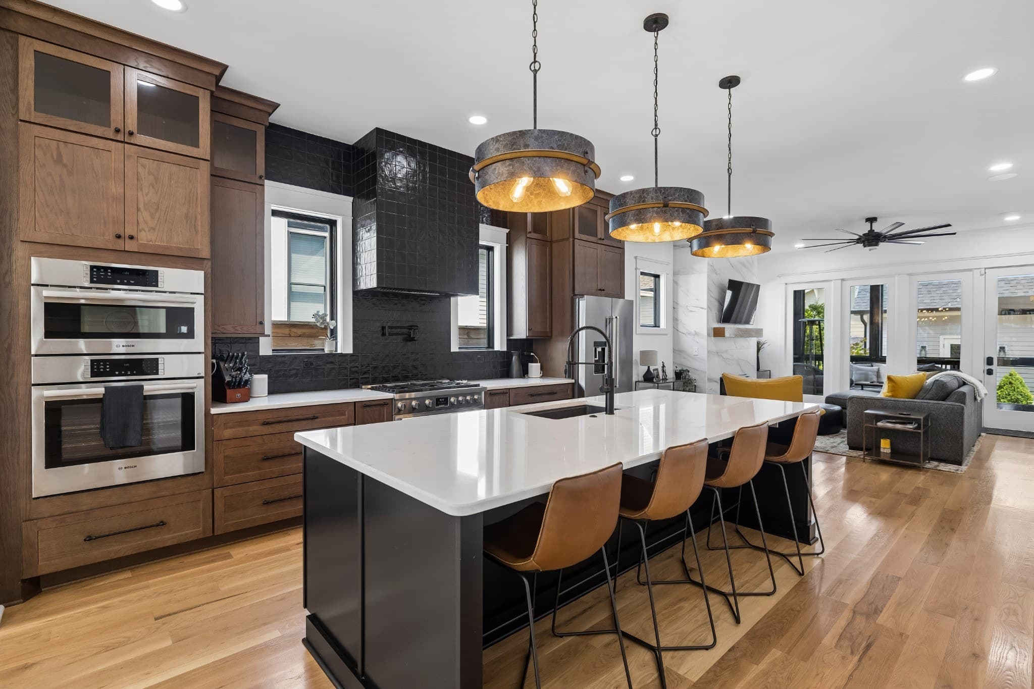 Kitchen with wood cabinets, a black tile backsplash and range hood, a stainless gas range, double wall ovens and a large island with four leather stools under three pendant lights at 1012 Lawrence Avenue in 12 South Nashville