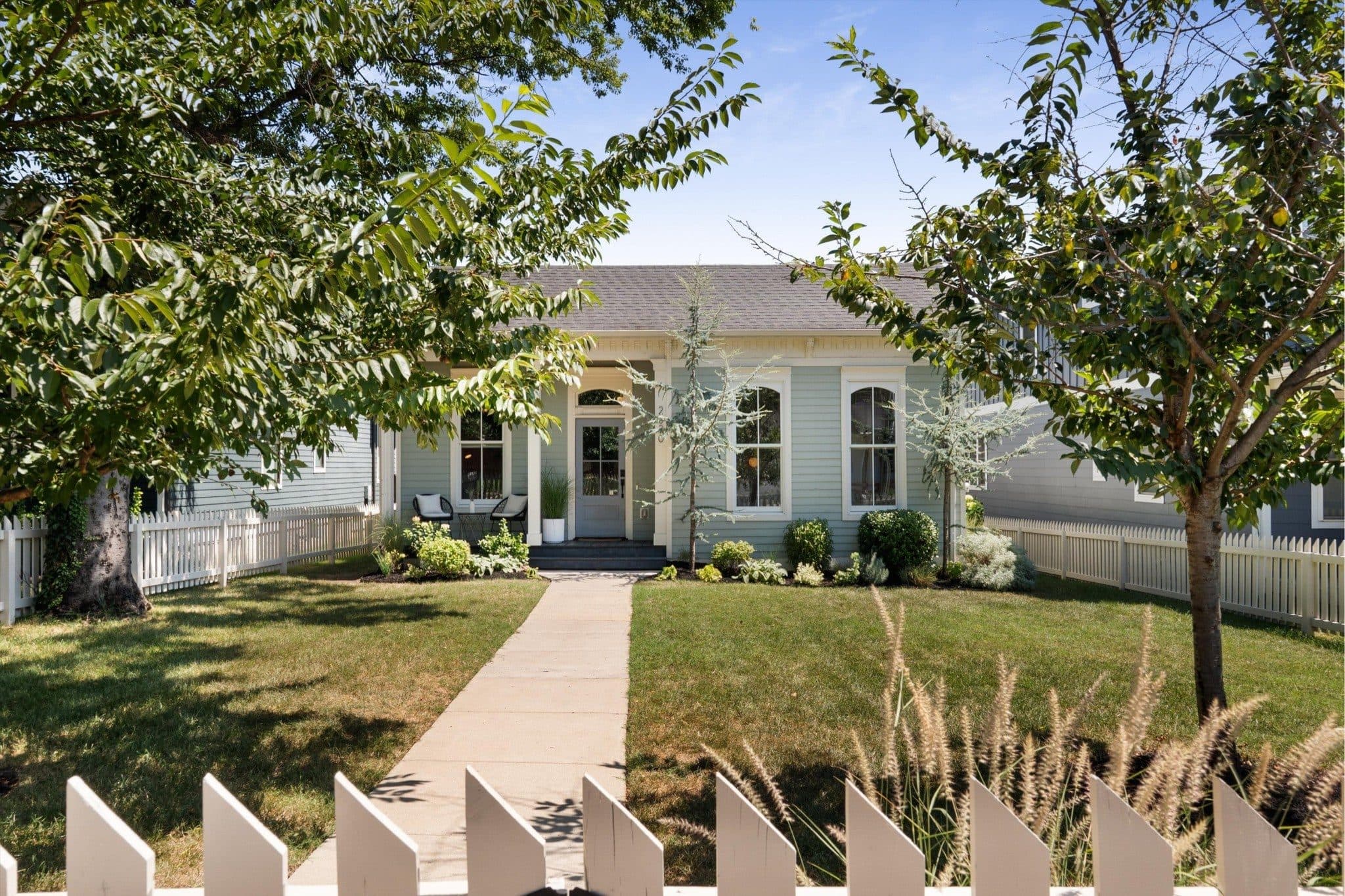 Front exterior of the sage Italianate with arched windows, a covered porch, and a white picket fence at 2020 10th Avenue South, one of the 12 South homes for sale in 12 South Nashville
