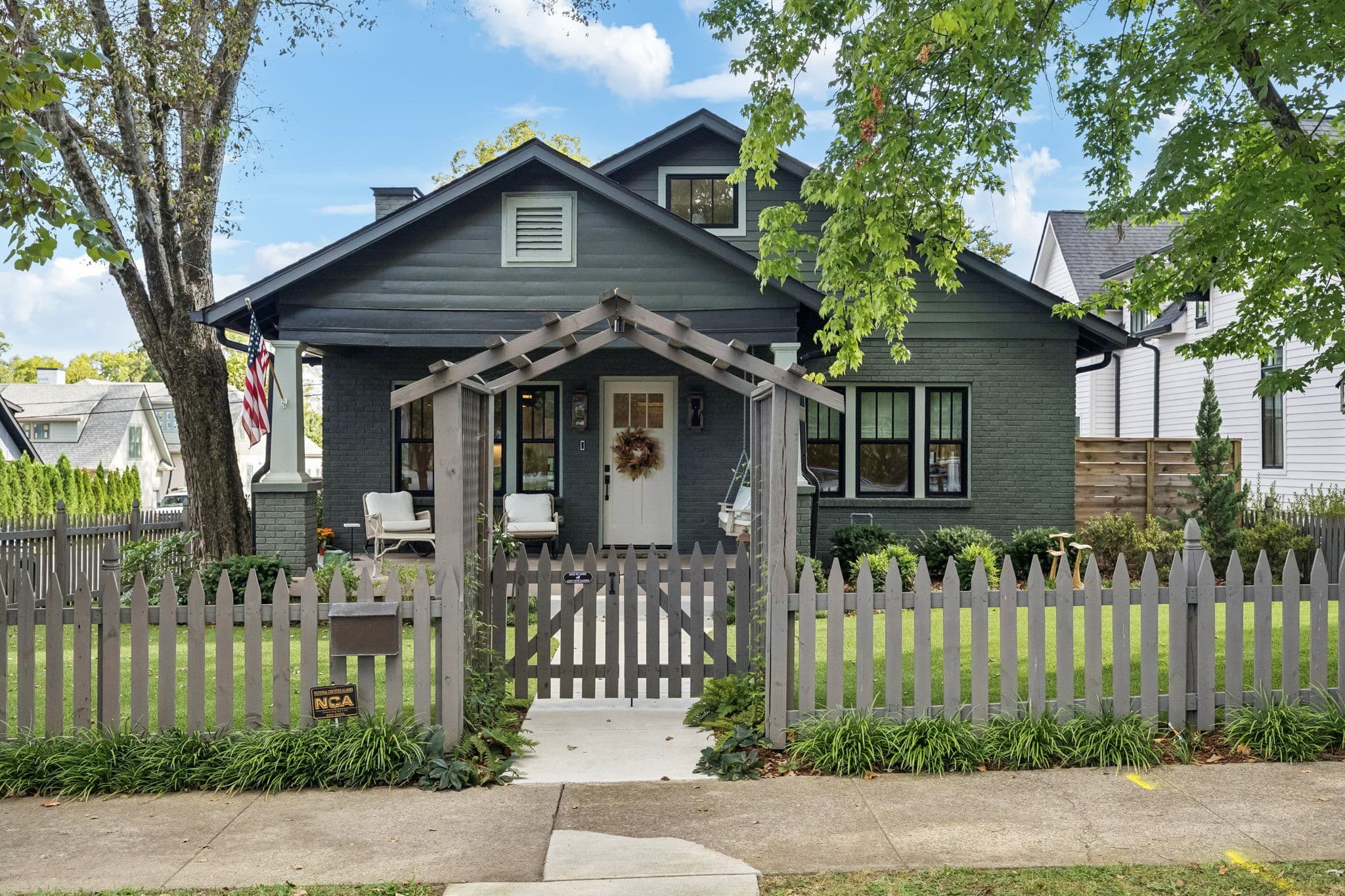Front exterior of the renovated dark brick bungalow with porch, picket fence, and arbor gate at 1101 Montrose Avenue, one of the 12 South homes for sale in Nashville
