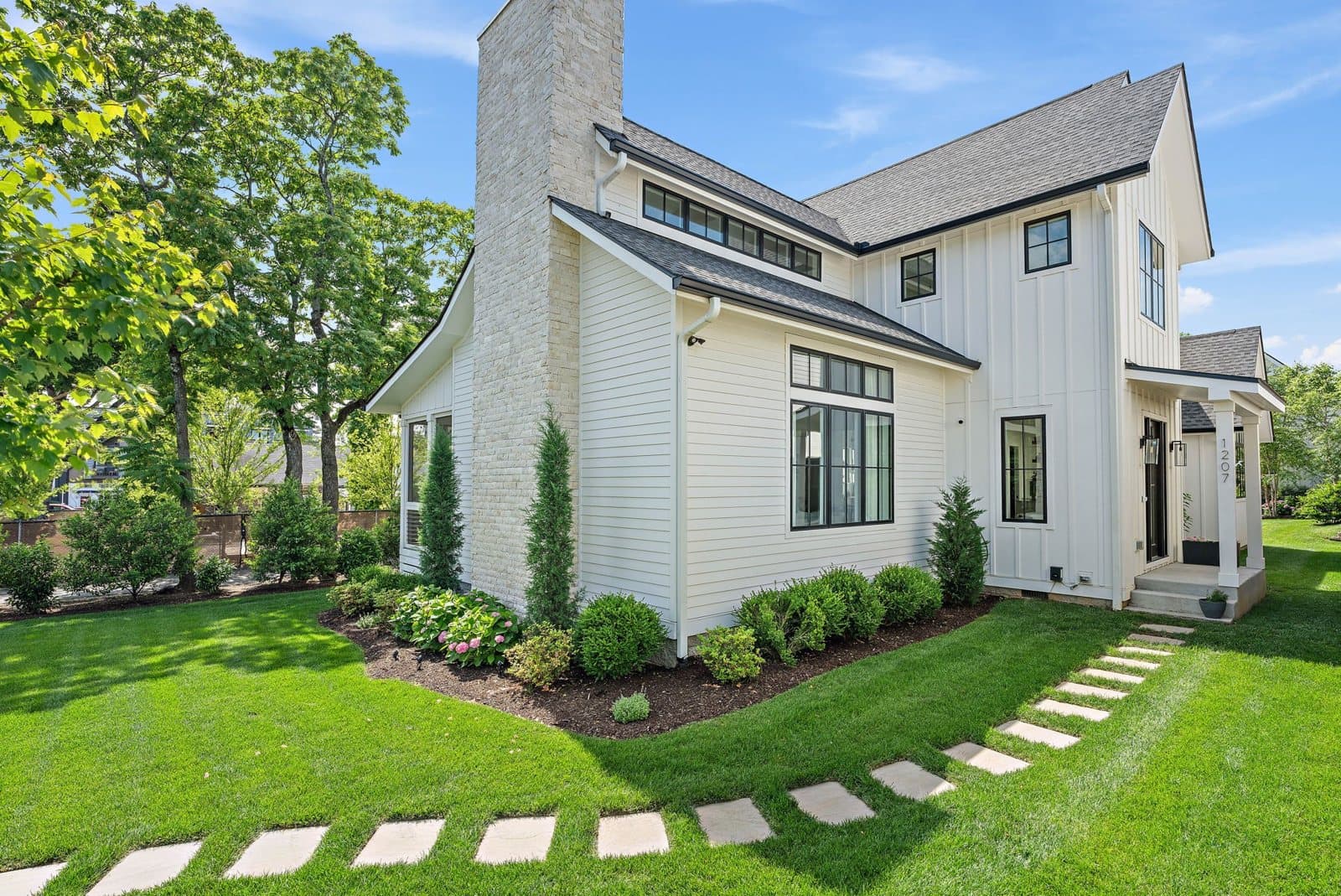 Exterior of 1207 Sweetbriar Ave, a white board and batten home with a stone chimney on a corner lot, one of the 12 South homes for sale in Nashville