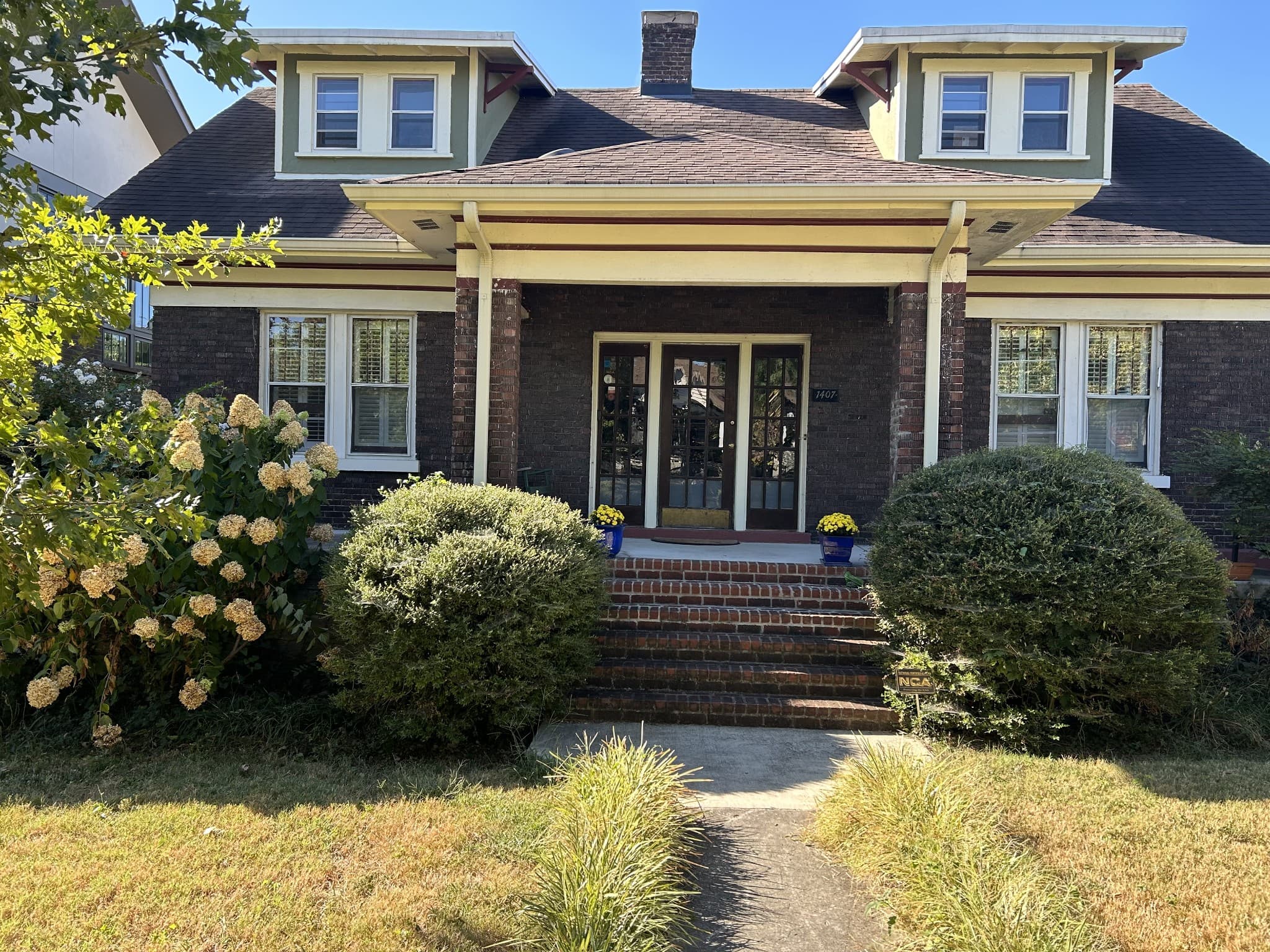 Front exterior of 1407 Elmwood Ave, a 1925 brick craftsman home with a wide front porch, brick steps, and two dormers, one of the 12 South homes for sale in Nashville