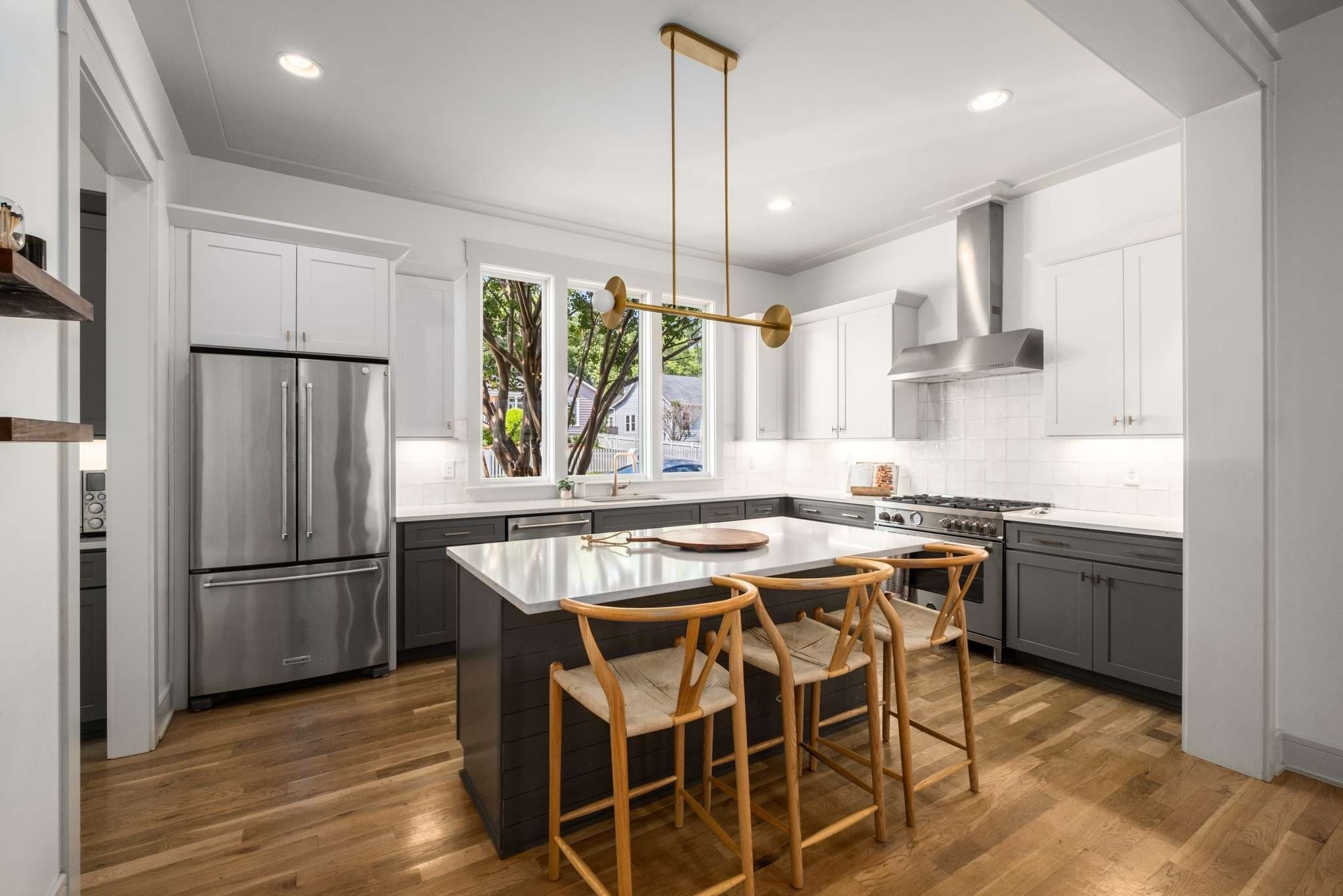Kitchen with white upper cabinets, gray lower cabinets, a center island with seating, a gas range with a stainless hood, a tile backsplash and a brass pendant light at 2018 10th Avenue South in 12 South Nashville