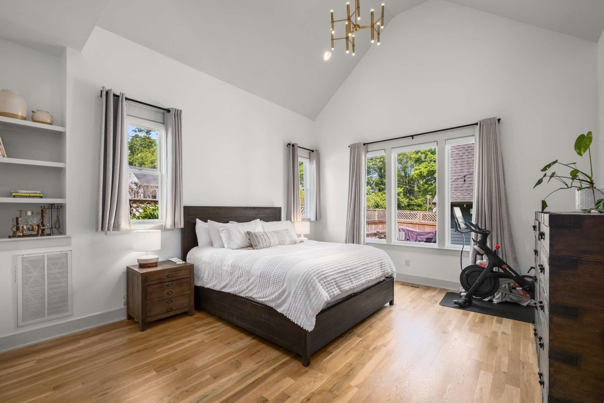 Main floor primary bedroom with a vaulted ceiling, a modern chandelier, built in shelves, hardwood floors and windows on two walls at 2018 10th Avenue South in 12 South Nashville