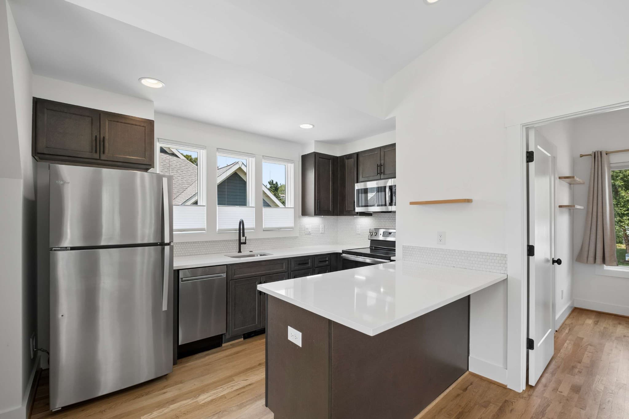Kitchen in the detached accessory dwelling unit with dark wood cabinets, stainless appliances, white counters, a peninsula and a row of windows at 2018 10th Avenue South in 12 South Nashville