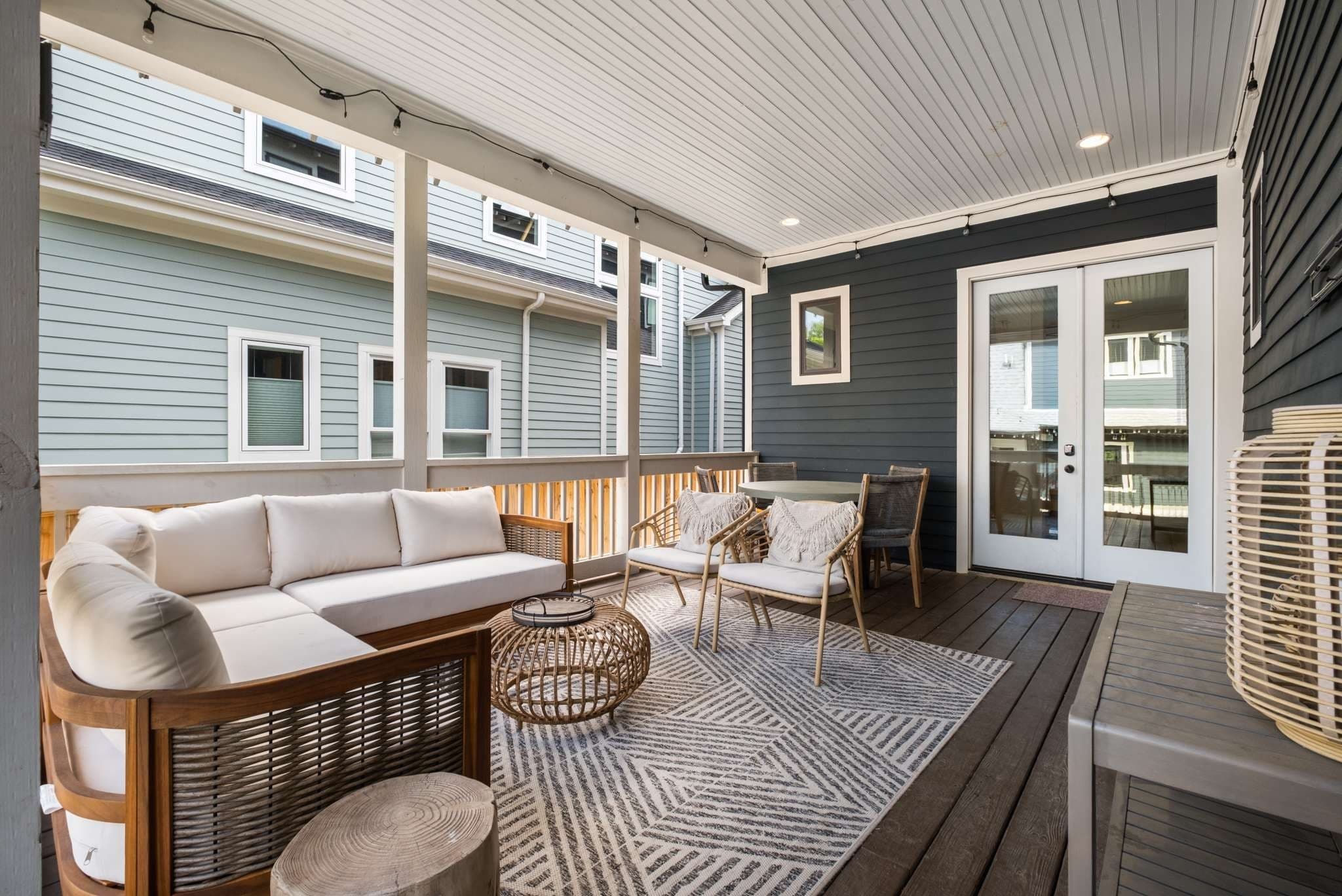 Covered rear porch with a sofa, lounge chairs, a dining table, string lights and French doors back into the house at 2018 10th Avenue South in 12 South Nashville