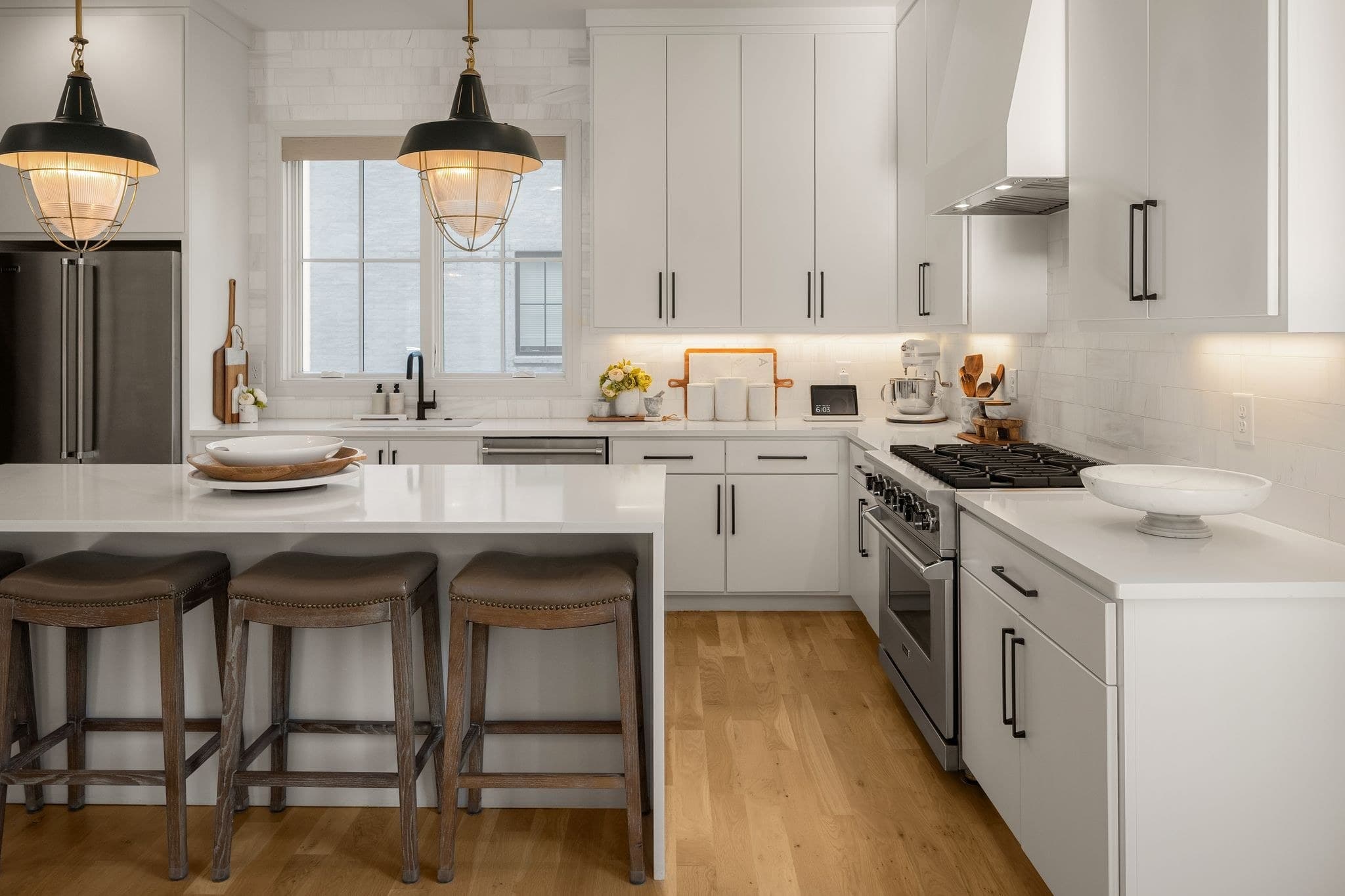 Kitchen with white ceiling height cabinetry, a waterfall island with three wood barstools, a Viking gas range, pendant lights and light hardwood floors at 2086 12th Avenue South in 12 South Nashville