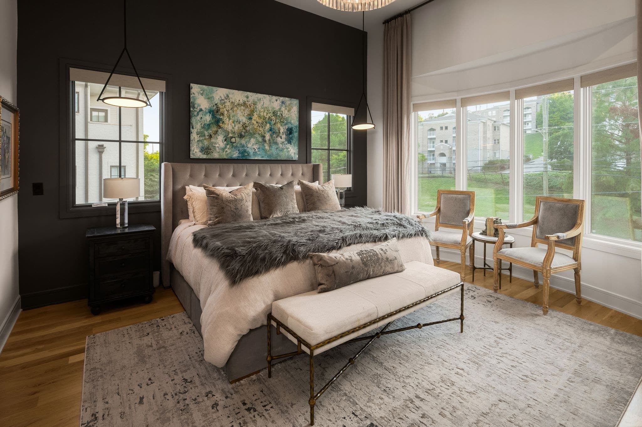 Upstairs primary bedroom with a dark accent wall, a tufted headboard, bay windows, an upholstered bench and two armchairs in the bay at 2086 12th Avenue South in 12 South Nashville