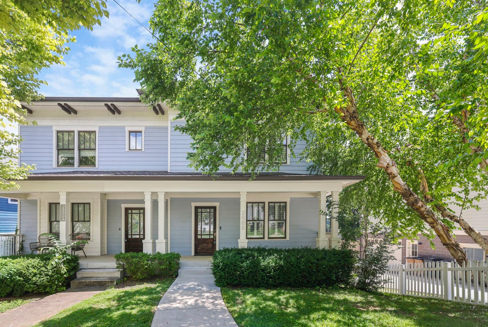 Front exterior of 2500B 9th Ave S, a two story home with a covered front porch and white picket fence, one of the 12 South homes for sale in Nashville