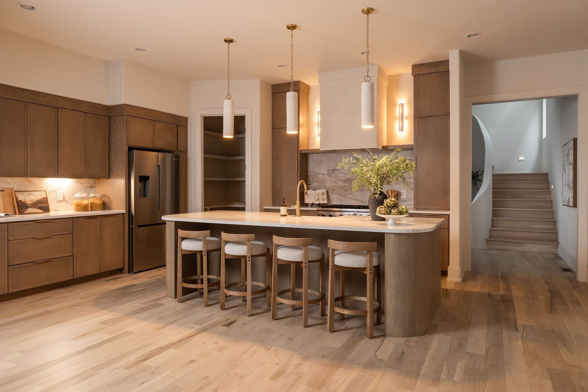 Kitchen with custom wood cabinets, a curved island with four stools, three pendant lights, and a view to the curved staircase at 2507A Vaulx Lane in 12 South Nashville