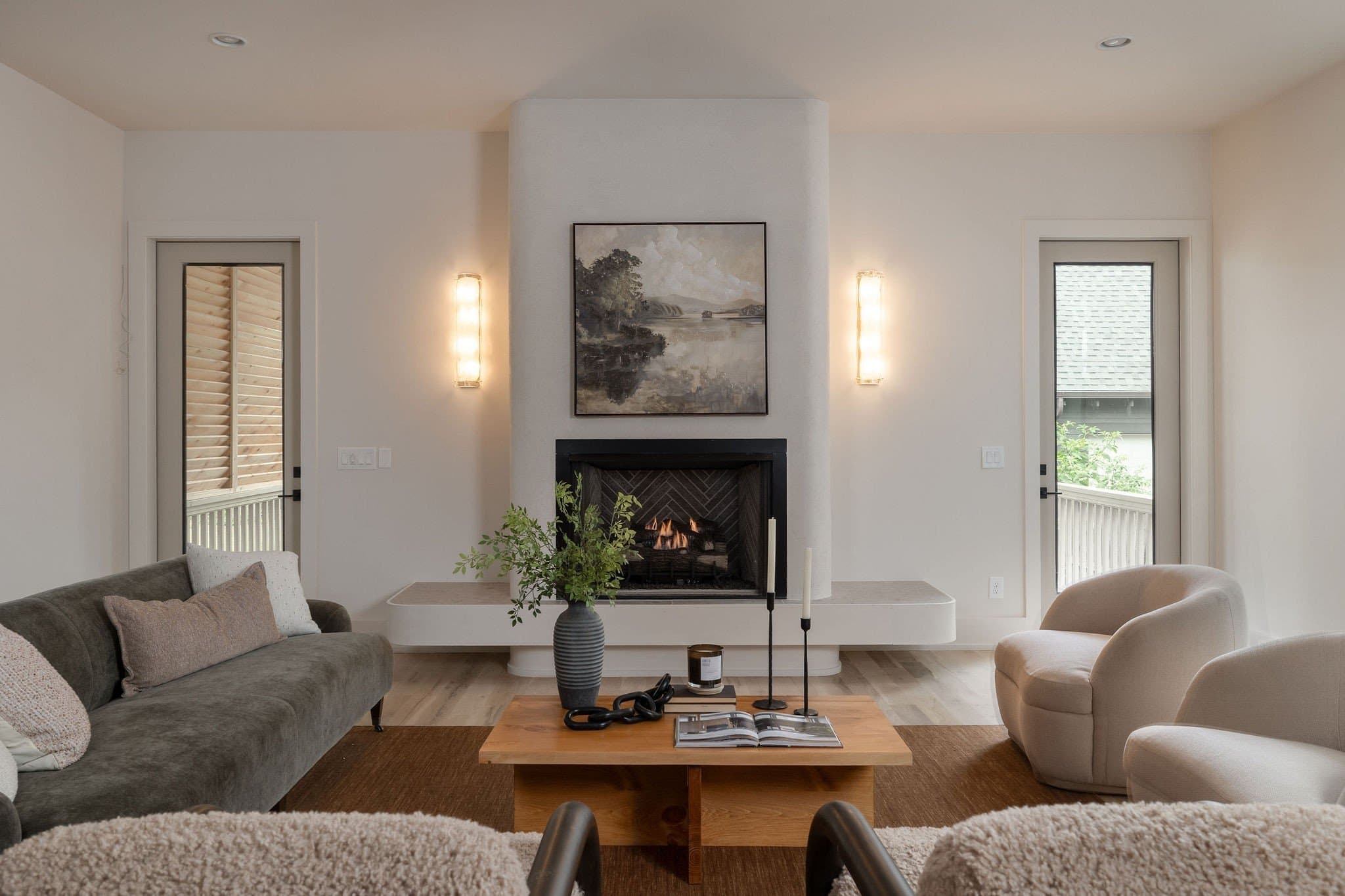 Living room with a curved stucco fireplace, frosted glass sconces, hardwood floors, and glass doors to the outside at 2507A Vaulx Lane in 12 South Nashville