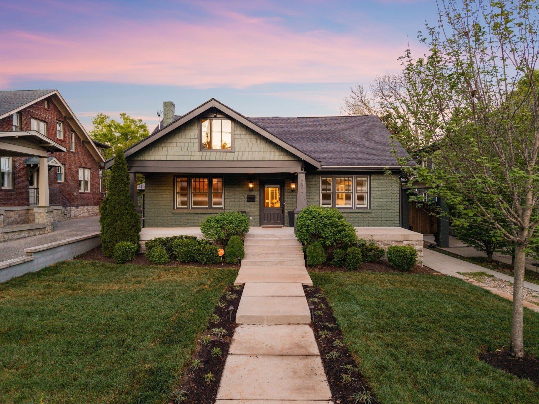 Front exterior of 2510 Belmont Boulevard at dusk, a 1928 home with green painted brick, a covered front porch and a long front walk, one of the 12 South homes for sale in Nashville