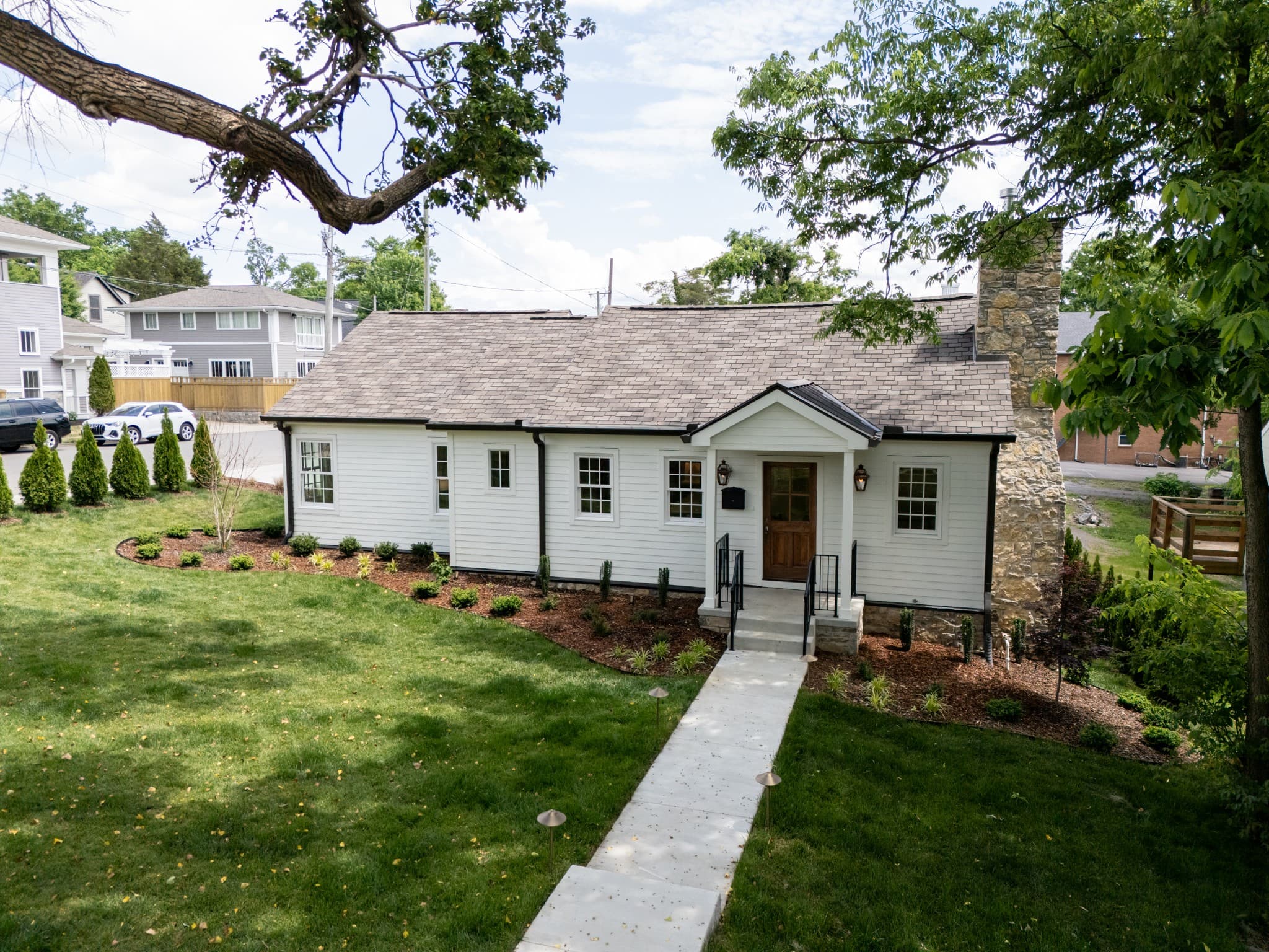 Front exterior of 2600 Belmont Blvd, a restored 1945 white home with a stone chimney on a corner lot, one of the 12 South homes for sale in Nashville