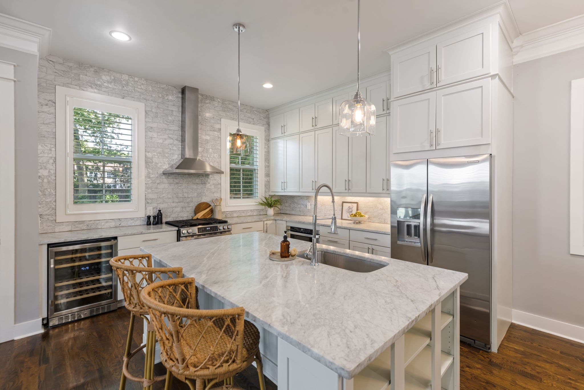 Kitchen with white cabinets, a marble topped island with two rattan stools, a stainless gas range under a chimney hood, a wine refrigerator and a stainless refrigerator at 908B Gale Lane in 12 South Nashville