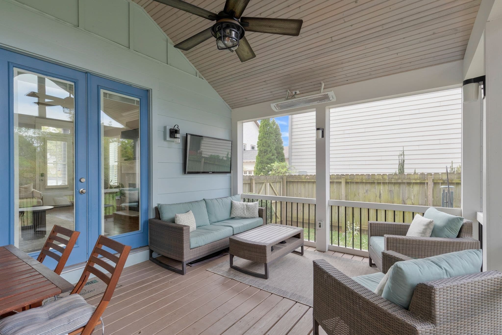 Screened porch with a wood plank ceiling, a ceiling fan, a mounted heater, wicker seating and blue French doors, with the fenced back yard beyond, at 908B Gale Lane in 12 South Nashville