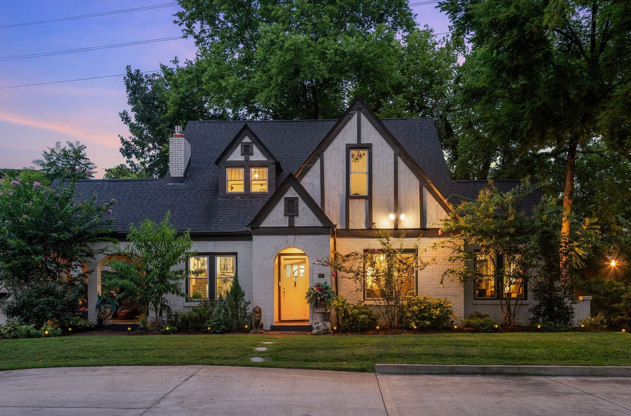Front exterior of 947 Gale Lane at dusk, a 1928 brick and stone Tudor with steep gables, an arched front door and a front lawn, one of the 12 South homes for sale in Nashville