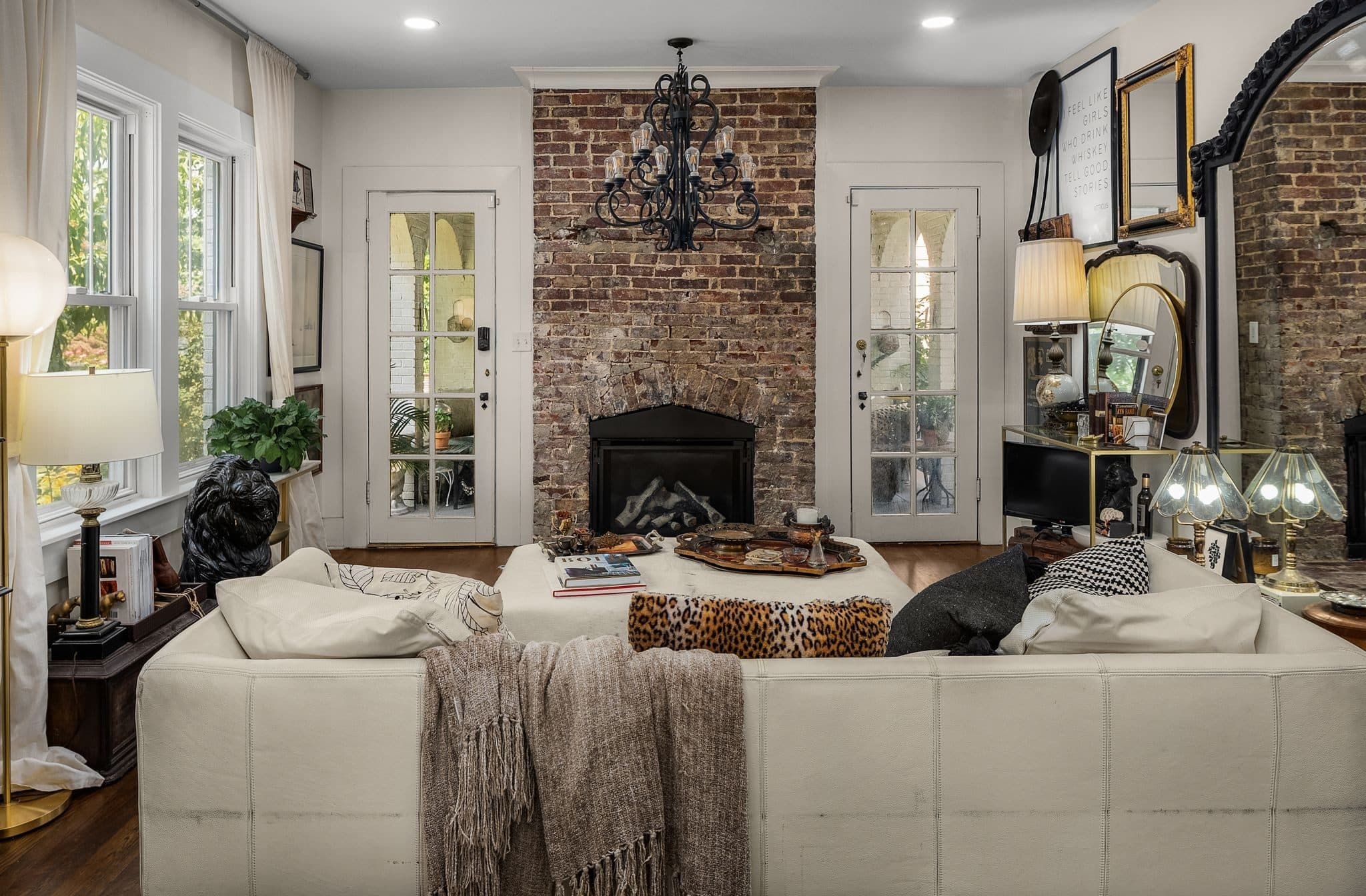 Living room with an exposed brick fireplace, an iron chandelier and glass paned doors on both sides at 947 Gale Lane in 12 South Nashville