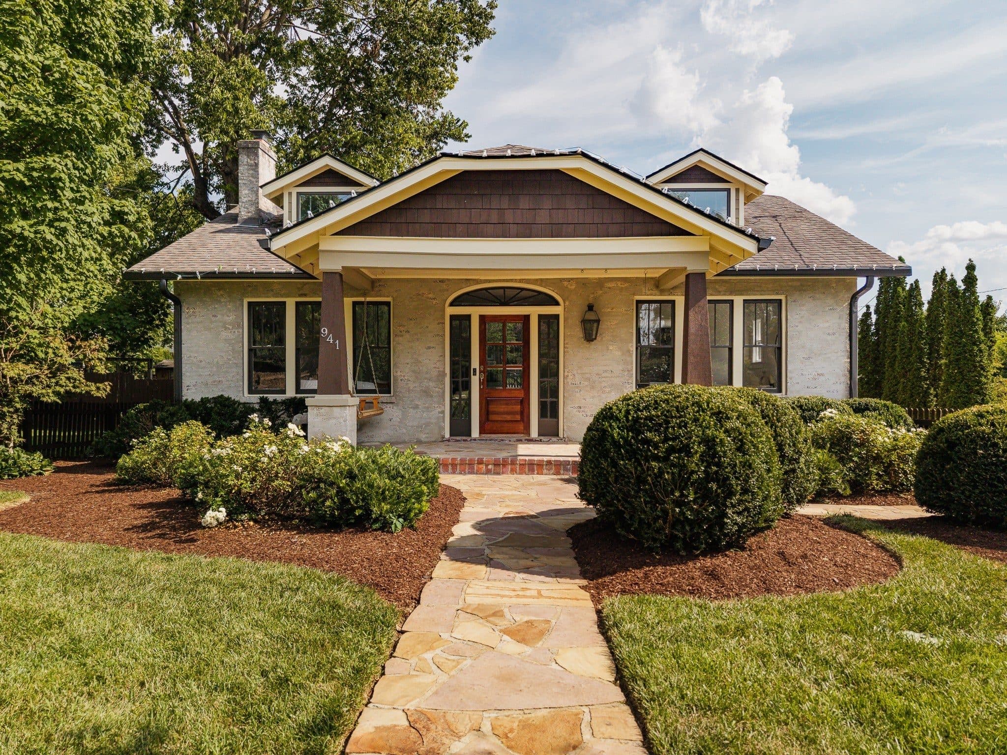 Front exterior of the light stone Craftsman with a covered porch and flagstone walk at 941 Inverness Avenue, one of the 12 South homes for sale in 12 South Nashville